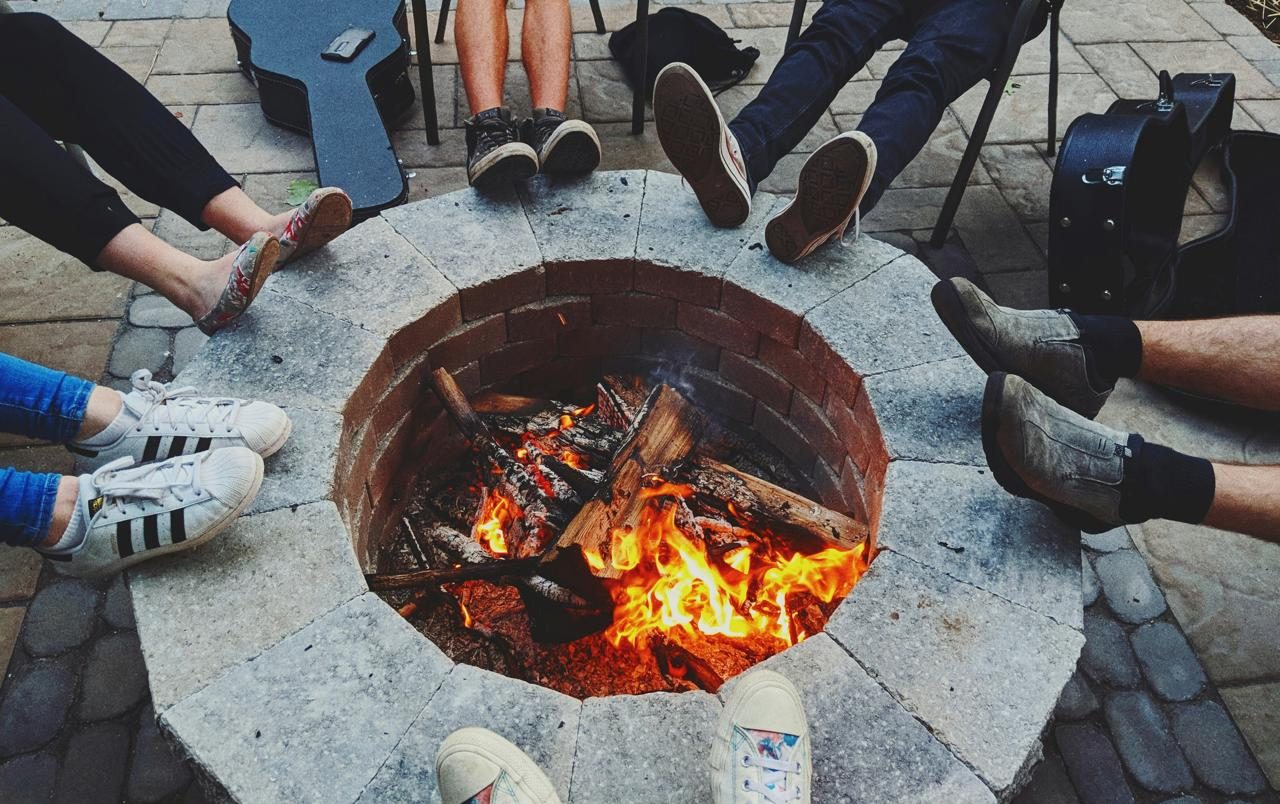 Friends with their feet up around a lit fire pit, guitars beside them