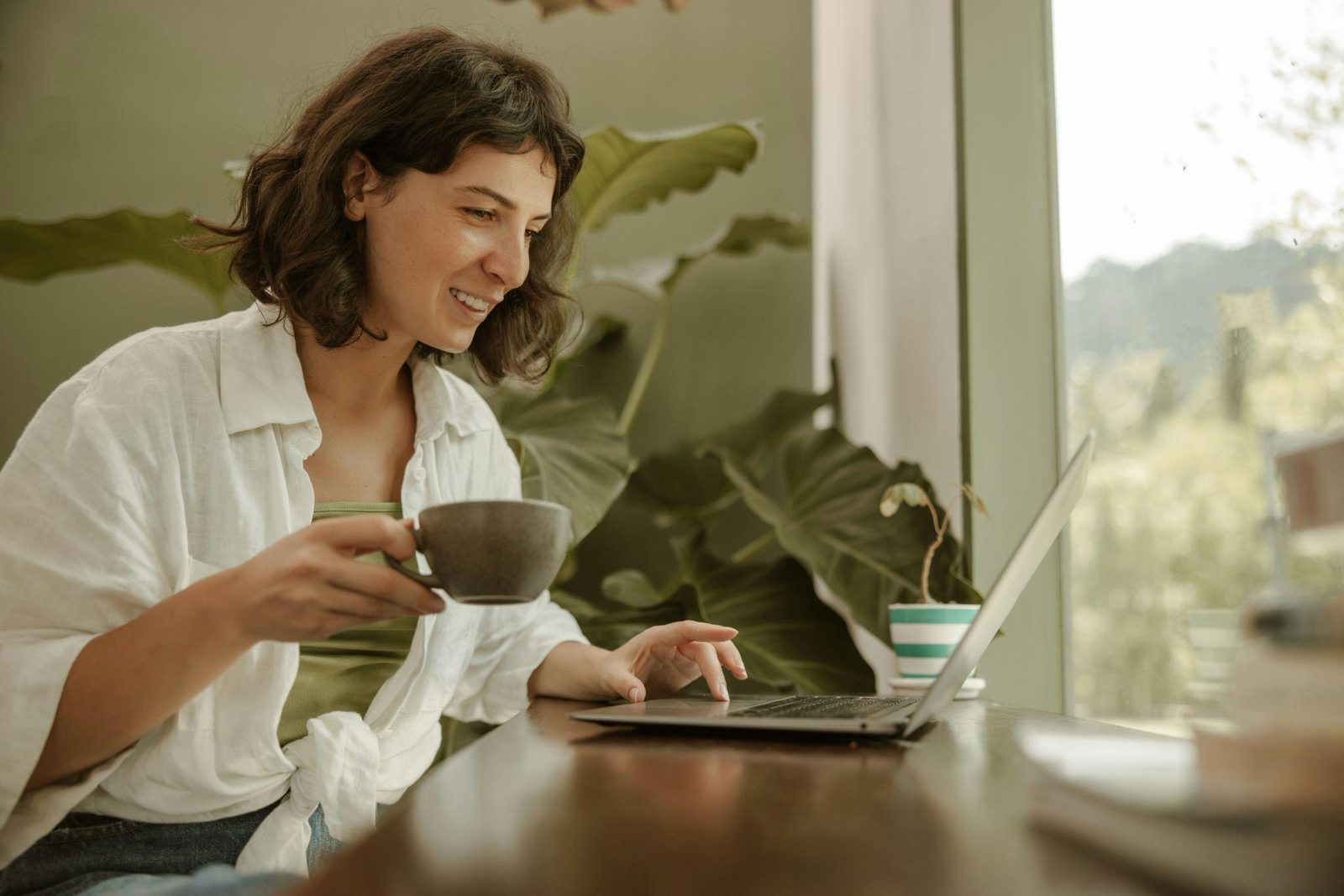 A woman at a laptop with a cup of tea, joining a session from home